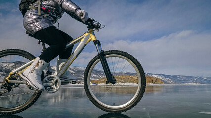 Woman is riding bicycle on the ice. Tires on bike are covered wi