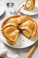 Freshly baked a showstopping raised pie using sausagemeat and boiled eggs on light gray background