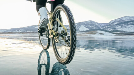 Woman is riding bicycle on the ice. Tires on bike are covered wi