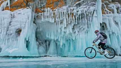 Woman is riding bicycle near the ice grotto. The rock with ice c - Powered by Adobe