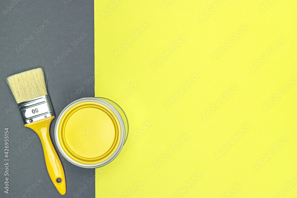 Wall mural can of yellow paint with yellow paintbrush on yellow-gray background. colors of the year.