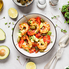 Easy grilled shrimp avocado salad with cherry tomatoes, capers and microgreens. Gray background. Top view.