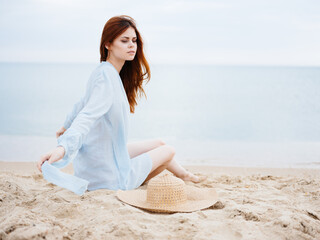 Fototapeta na wymiar A woman in a blue dress on the sand and a hat in the hand of the ocean sea