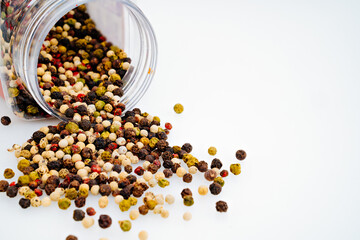 a mixture of peppers is scattered from a jar on a white background.