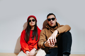 Fashionable young couple in sunglasses and hoodies sitting on the floor.