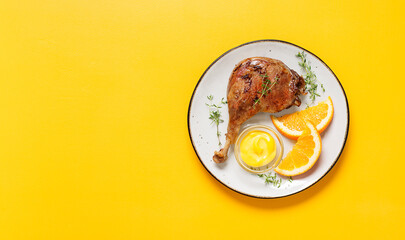 Duck leg confit served with orange wedges and mustard sauce .Traditional french cuisine.Yellow background, top view. Space for text.