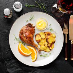 Duck leg confit served with potato chips and mustard sauce .Traditional french cuisine. Black background, top view. 	