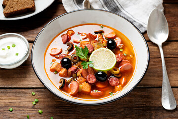 Traditional Russian meat soup Solyanka in bowl on rustic wooden table. 