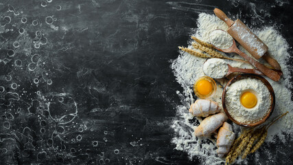 Bakery background. Flour, eggs, rolling pin for dough on a black background. Top view. Free space...