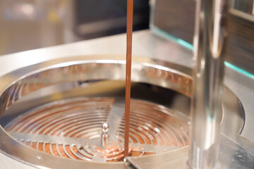 melted chocolate dripping from the tap fountain confectioner filling candy mold with chocolate at confectionery shop