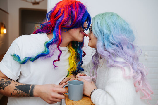 Bizzare looking couple in colorful wigs and sunglasses. Man licks girl's nose.
