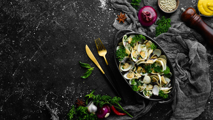 Boiled shellfish in shells with garlic and parsley in a black plate. Seafood. Top view. Free space for text.