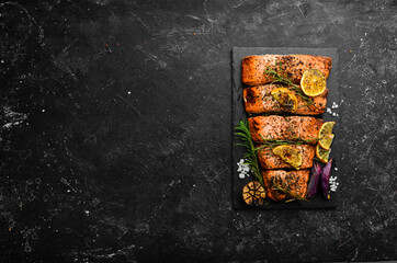 Fototapeta Salmon. Pieces of grilled fish on a black stone background. Recipe. Seafood. Free space for text. obraz