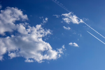 White clouds in a blue sky with traces of an airplane. Inversion trail in the sky