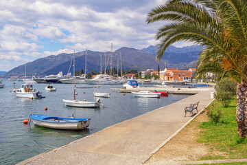 Fototapeta na wymiar Beautiful Mediterranean landscape with village embankment and fishing boats on water. Montenegro, Adriatic Sea, view of Bay of Kotor and Seljanovo village near Tivat city