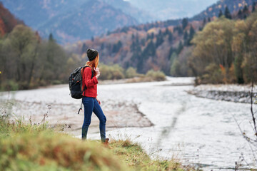 Naklejka premium young woman with backpack in the mountains autumn travel tourism landscape shallow water river
