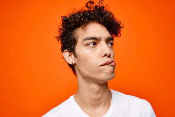 Obraz premium cute guy in white t-shirt curly hair grimace orange background