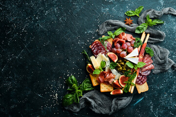A plate with cheese, salami, prosciutto and snacks on a black stone plate. Antipasto. Top view. Italian food. Free space for your text.