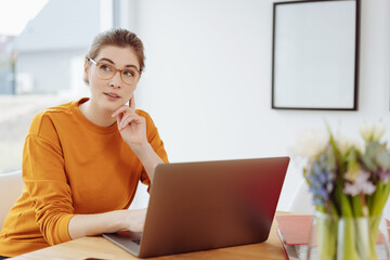 Young woman sitting pondering a problem as she works at her laptop