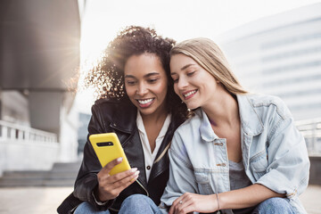 Young women friends using smartphone in a city, Cute smiling girls having fun using mobile phone on...