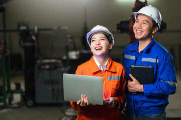 portrait of asian emgineer male female technician in safty uniform standing and turn around to look at camera and laugh smile with cheerful and confident in machinery factory workplace background