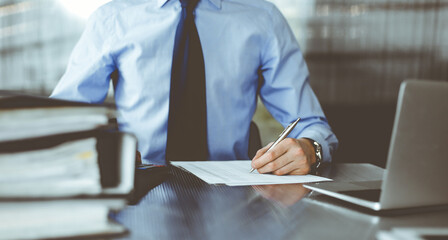 Unknown man accountant in blue shirt use calculator and computer with holding pen on while staying...