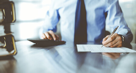 Unknown man accountant in blue shirt use calculator and computer with holding pen on while staying at home during covid pandemic. Taxes and audit concept