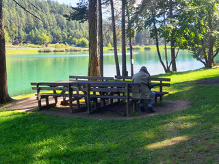 A lonely old man sits on a bench near lake in Coredo and Tavon.