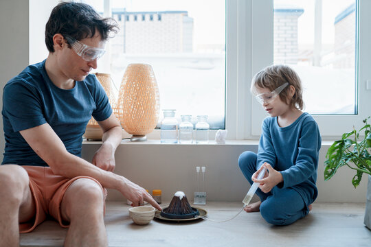 Dad And Son Making Chemical Experiment Using A Mock Volcano, Baking Soda And Vinegar. Home Learning