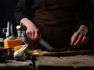 Chef cuts blackberries for cooking meat or salad on the background of ingredients.Various cheeses, garlic, tomatoes and spices.Culinary recipes