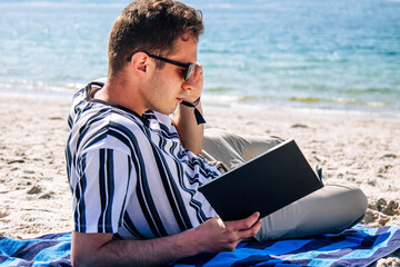 man lying relaxed on his towel on the beach reading a book