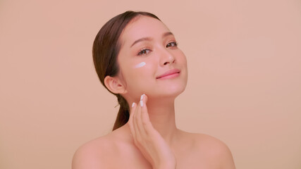 Beautiful face of Asian young woman with natural skin. Portrait of a girl applying moisturizer cream onto her face.