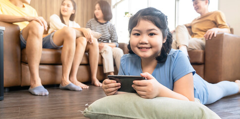 Fototapeta premium asian daughter child concentrate focus hand use smartphone game online playing with cheerful and fun quarantine stay home in living room home interior background