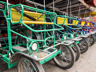 Fototapeta na wymiar Italian cycle rickshaws are in a row for rent in the park. Active lifestyle while pedaling. Yellow, blue, green. Metal frame