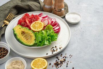 Healthy salad with fresh ingredients, avocado, radish, tomato lettuce on a gray concrete background.