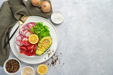 Vitamin-rich, healthy salad with avocado, tomato, radish and lettuce on a light gray background with space to copy.