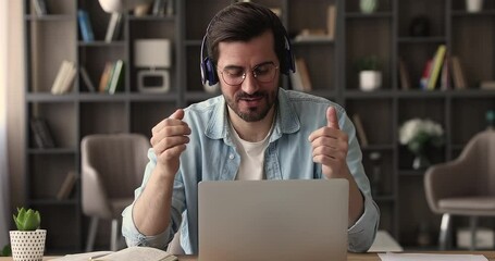 Happy young man in eyeglasses wearing wireless headphones, enjoying online video call using computer zoom application. Smiling 30s manager communicating distantly with colleagues at web camera meeting - Powered by Adobe