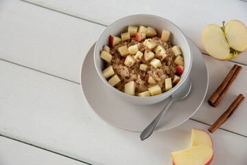 Oatmeal with apple pieces and cinnamon in a gray deep plate on a white wooden background close up side view
