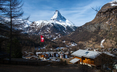 mountain village Zermatt under Matterhorn in snow in bright sunny day with flag 