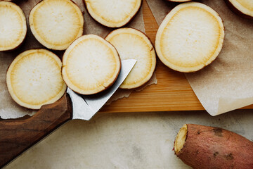 knife cuts batata on round slices with skin of raw red sweet potatoes on baking paper. cooking homemade simple food, Yam recipes . selective focus