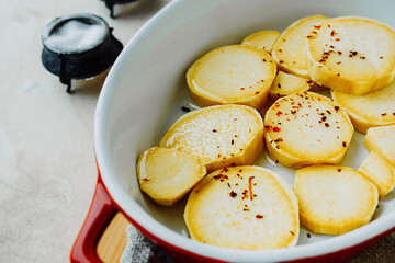 round slices raw red sweet potatoes in red ceramic baking dish, spices, salt, pepper. process cooking homemade food. yam recipes, food content, life atmosphere, selective focus
