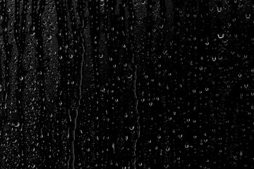 Naklejka na ściany i meble Drops of water flow down the surface of the clear glass on a black background. Texture for creativity.