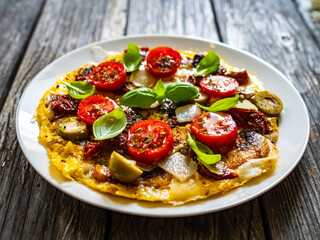 Delicious breakfast - scrambled eggs with onion, sun dried tomato, basil, parmesan and green olives on wooden table
