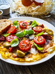 Delicious breakfast - scrambled eggs with onion, sun dried tomato, basil, parmesan and green olives on wooden table
