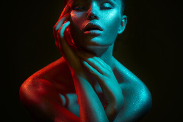 Fashion model woman in colorful bright sparkles and neon lights posing in studio, on black,...