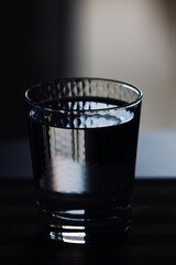 High angle close up of a glass of water left in dark. Still water in honeycomb textured transparent glass.
