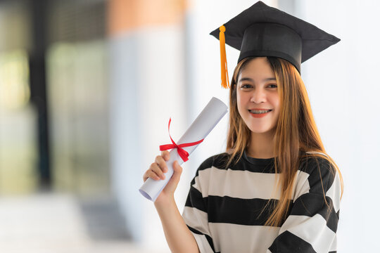 Young asian woman university graduates in graduation gown and mortarboard holds a degree certificate celebrates education achievement in the university campus.  Education stock photo