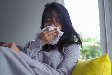 An Asian woman sick on the sofa in the house. Women have headaches, high fever and runny nose due to flu. The concept of illness with influenza