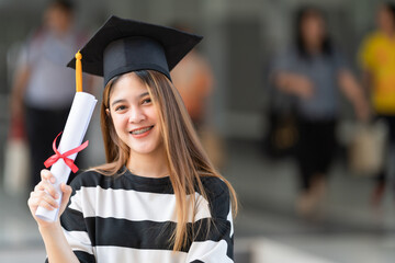 Young asian woman university graduates in graduation gown and mortarboard holds a degree certificate celebrates education achievement in the university campus.  Education stock photo
