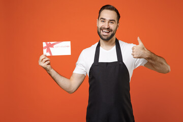 Young happy fun man 20s barista bartender barman employee wearing black apron white t-shirt work in coffee shop hold gift voucher flyer mock up isolated on orange background Small business startup